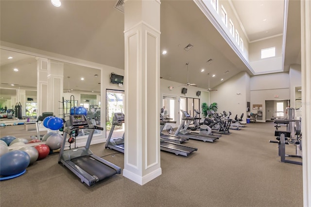 gym with a towering ceiling, decorative columns, ceiling fan, and a healthy amount of sunlight