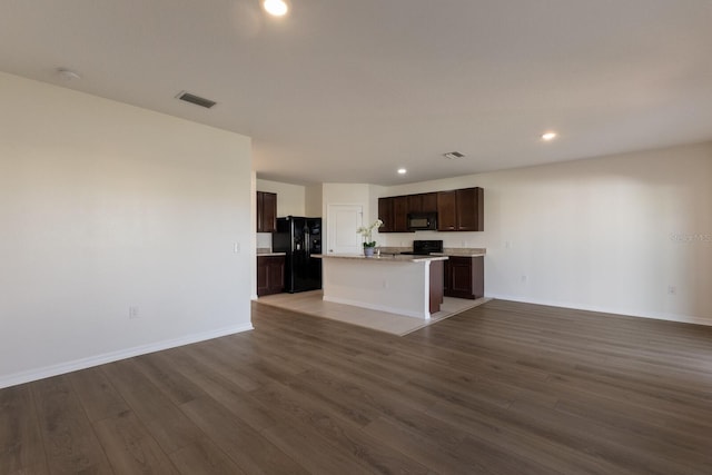 kitchen featuring dark brown cabinetry, dark hardwood / wood-style flooring, an island with sink, and black appliances