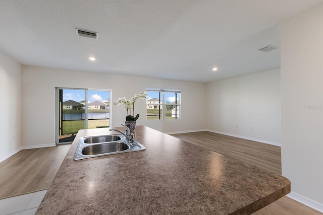 kitchen featuring sink, light hardwood / wood-style flooring, a textured ceiling, and a water view