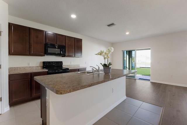 kitchen featuring sink, light hardwood / wood-style flooring, dark brown cabinets, a kitchen island with sink, and black appliances