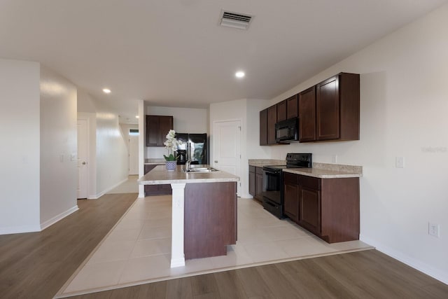 kitchen featuring dark brown cabinets, a kitchen island with sink, light wood-type flooring, and black appliances