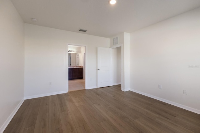 unfurnished bedroom with ensuite bath and dark wood-type flooring