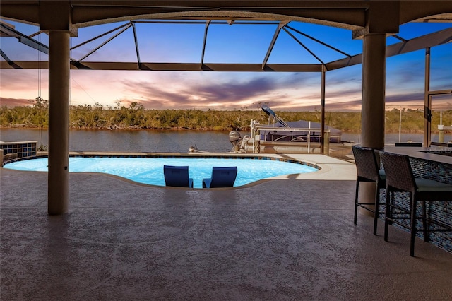 pool at dusk featuring a water view and a patio