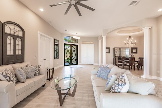 living room featuring light wood-type flooring, ceiling fan with notable chandelier, and ornate columns