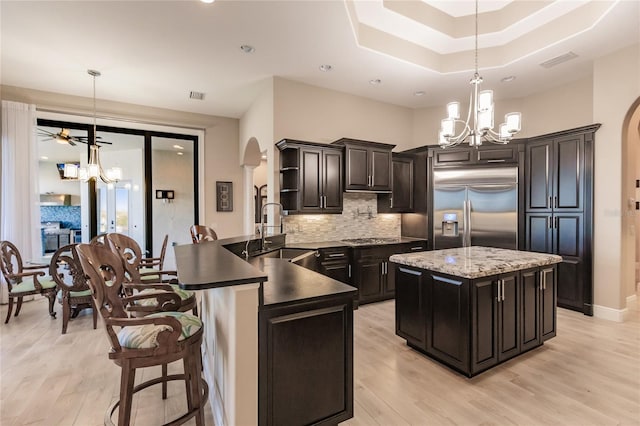 kitchen with sink, stainless steel built in refrigerator, kitchen peninsula, pendant lighting, and ceiling fan with notable chandelier