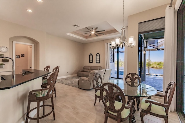 dining space featuring light wood-type flooring, ceiling fan with notable chandelier, a raised ceiling, and sink