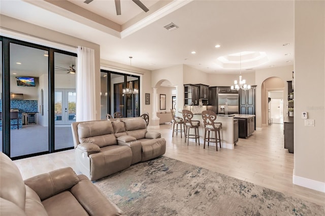 living room featuring an inviting chandelier, light wood-type flooring, french doors, and a tray ceiling