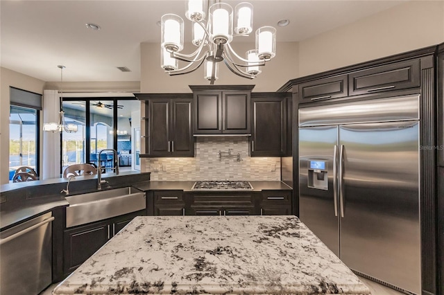 kitchen with tasteful backsplash, ceiling fan with notable chandelier, stainless steel appliances, sink, and decorative light fixtures