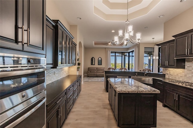 kitchen with an inviting chandelier, a raised ceiling, backsplash, a kitchen island, and appliances with stainless steel finishes