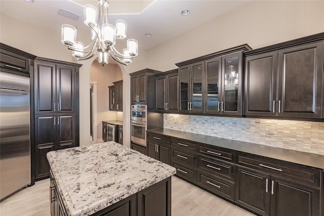 kitchen with hanging light fixtures, decorative backsplash, light wood-type flooring, a kitchen island, and stainless steel appliances