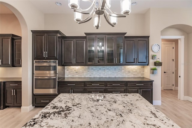 kitchen with stainless steel double oven, hanging light fixtures, an inviting chandelier, backsplash, and light wood-type flooring