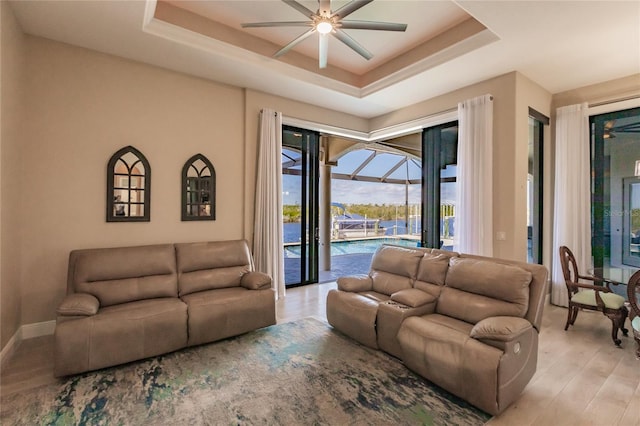 living room featuring ceiling fan, light hardwood / wood-style flooring, and a tray ceiling