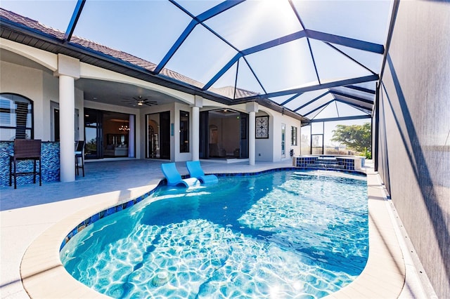 view of pool with glass enclosure, an outdoor bar, a jacuzzi, ceiling fan, and a patio