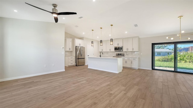 kitchen with stainless steel appliances, decorative light fixtures, white cabinets, lofted ceiling, and an island with sink