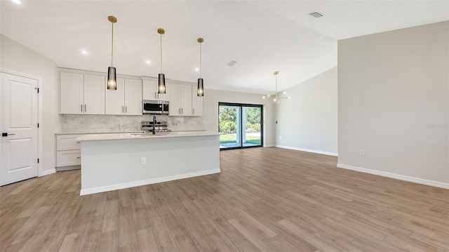 kitchen with lofted ceiling, hanging light fixtures, light hardwood / wood-style flooring, appliances with stainless steel finishes, and white cabinetry