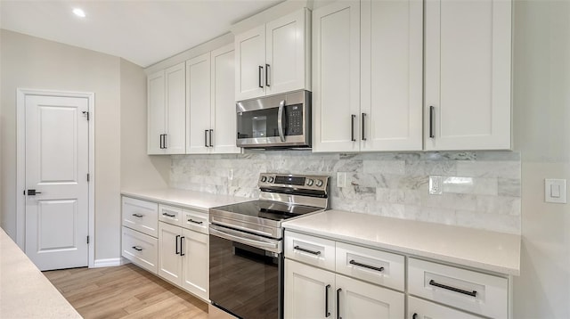 kitchen with white cabinetry, light hardwood / wood-style flooring, backsplash, vaulted ceiling, and appliances with stainless steel finishes