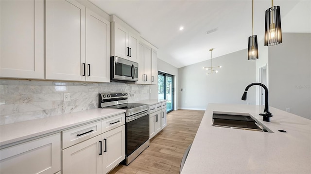 kitchen with sink, decorative light fixtures, vaulted ceiling, white cabinets, and appliances with stainless steel finishes