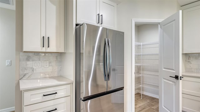 kitchen with stainless steel refrigerator, light stone countertops, backsplash, white cabinets, and light wood-type flooring