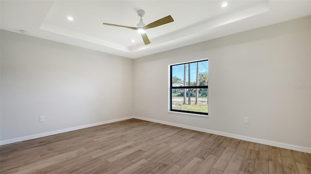 spare room featuring a tray ceiling, ceiling fan, and light hardwood / wood-style floors