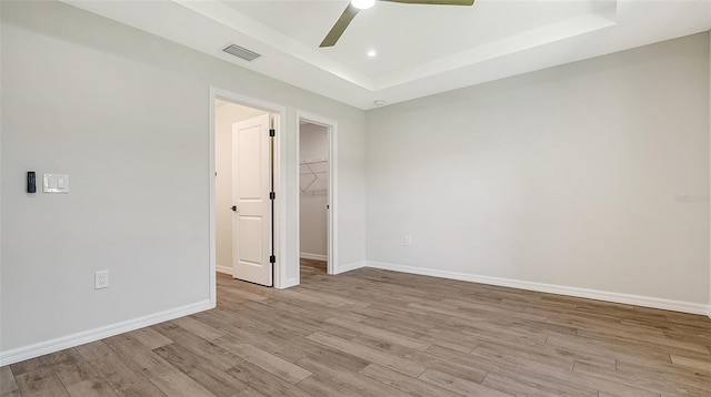 empty room featuring a tray ceiling, ceiling fan, and light hardwood / wood-style flooring