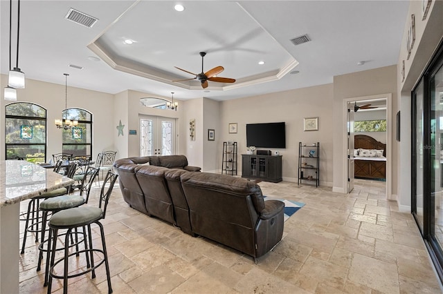 living room with french doors, ceiling fan with notable chandelier, a tray ceiling, and plenty of natural light