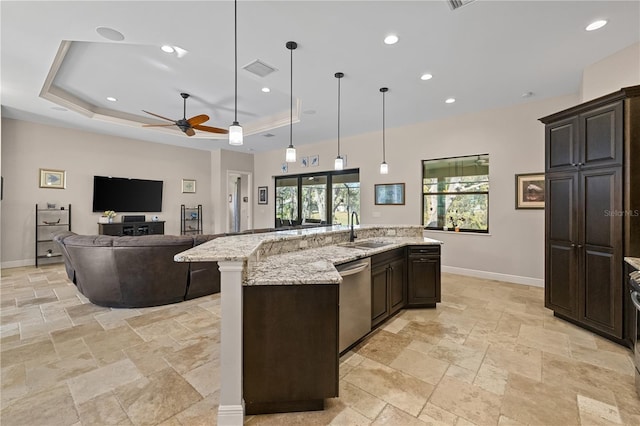 kitchen with a large island with sink, a raised ceiling, sink, stainless steel dishwasher, and ceiling fan