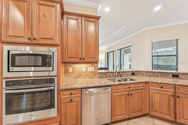 kitchen with appliances with stainless steel finishes, light stone counters, ornamental molding, sink, and light tile patterned floors