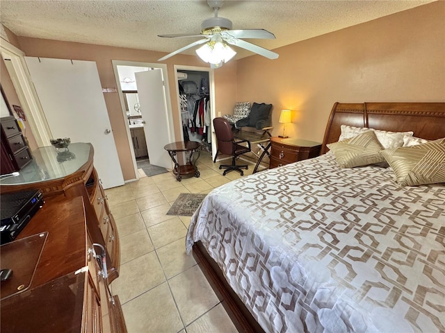 tiled bedroom with a walk in closet, ceiling fan, a textured ceiling, connected bathroom, and a closet