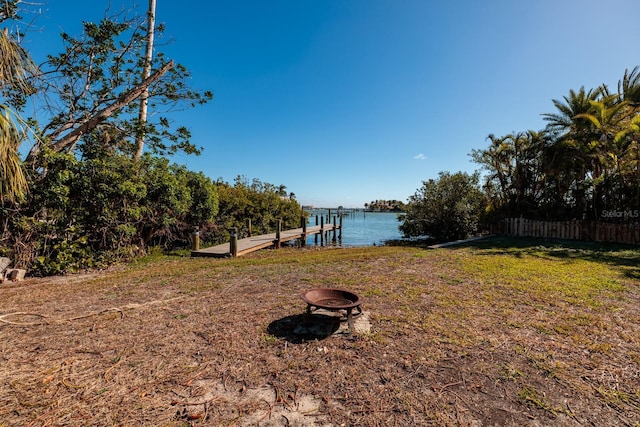 view of yard with a water view, a dock, and an outdoor fire pit