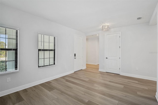 empty room featuring light wood-type flooring, an inviting chandelier, and a wealth of natural light