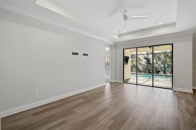 unfurnished room featuring wood-type flooring, a tray ceiling, ceiling fan, and crown molding