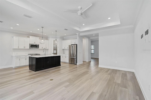 kitchen featuring white cabinets, decorative light fixtures, stainless steel appliances, and an island with sink