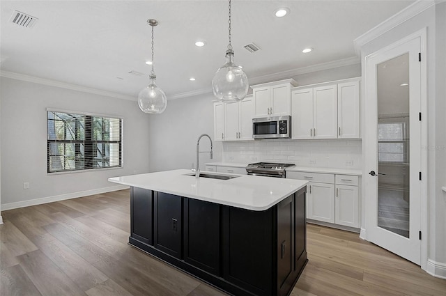 kitchen with pendant lighting, backsplash, white cabinets, a center island with sink, and stainless steel appliances