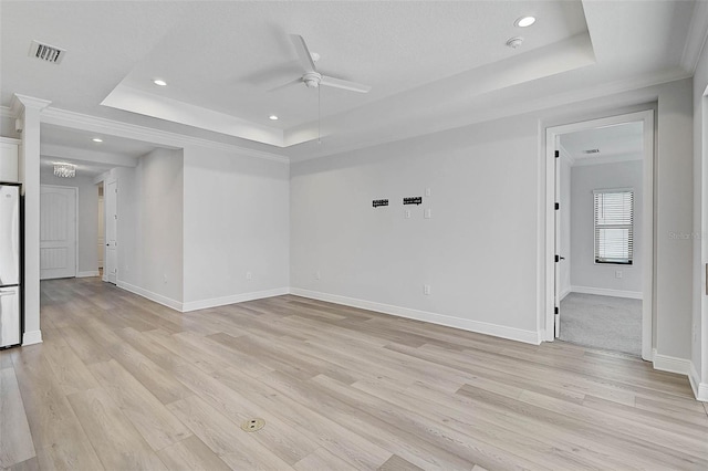 empty room featuring a tray ceiling, crown molding, light hardwood / wood-style floors, and ceiling fan with notable chandelier