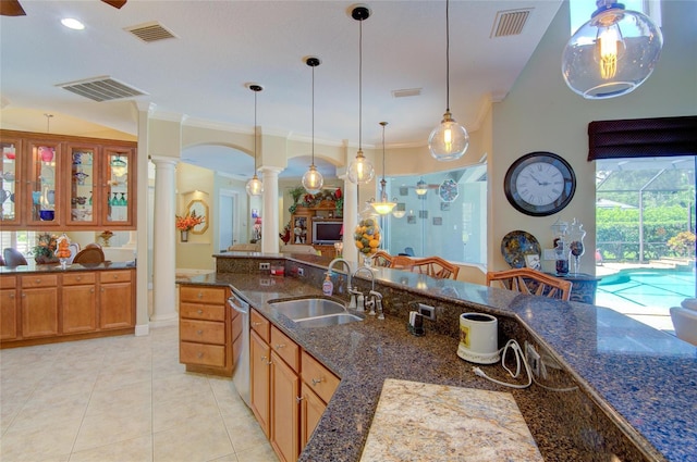 kitchen with sink, decorative columns, dark stone counters, pendant lighting, and ornamental molding