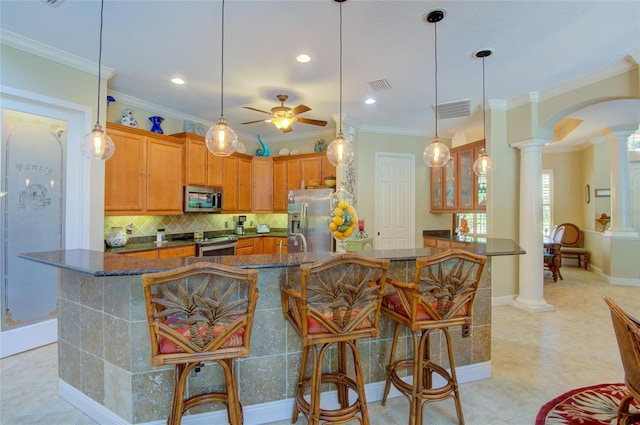 kitchen with ornate columns, ceiling fan, a kitchen breakfast bar, appliances with stainless steel finishes, and ornamental molding