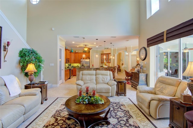 carpeted living room with ceiling fan, crown molding, and a high ceiling