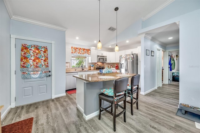 kitchen with stainless steel appliances, vaulted ceiling, decorative light fixtures, white cabinets, and a center island