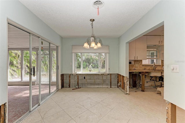 dining area featuring a wealth of natural light, sink, a textured ceiling, and a notable chandelier