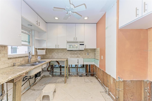 kitchen with sink, decorative backsplash, ceiling fan, light stone countertops, and white cabinetry