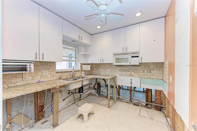 kitchen featuring light stone countertops, backsplash, ceiling fan, sink, and white cabinets