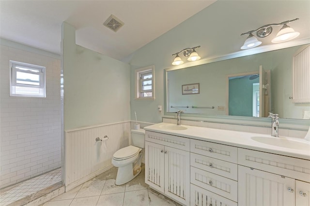 bathroom featuring a tile shower, a wealth of natural light, vanity, and toilet