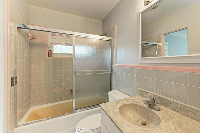 full bathroom featuring toilet, combined bath / shower with glass door, tile walls, and vanity