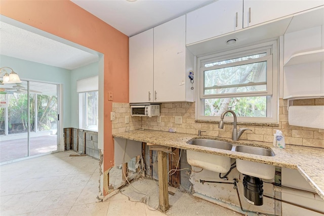 kitchen with sink, light stone counters, white cabinetry, and backsplash