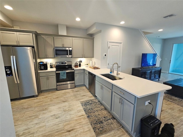 kitchen with kitchen peninsula, appliances with stainless steel finishes, light wood-type flooring, gray cabinetry, and sink