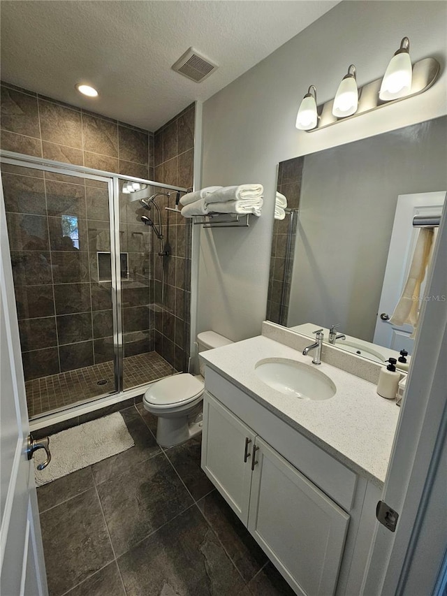 bathroom featuring vanity, toilet, a shower with door, and a textured ceiling