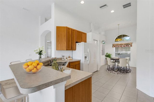 kitchen with sink, white fridge with ice dispenser, light tile patterned floors, kitchen peninsula, and a breakfast bar area