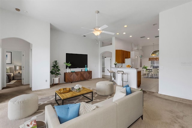 living room featuring ceiling fan, light colored carpet, and a towering ceiling