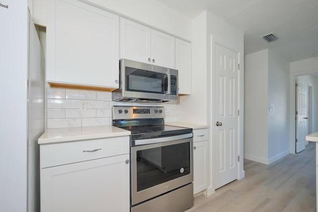 kitchen featuring white cabinets, appliances with stainless steel finishes, decorative backsplash, and light hardwood / wood-style flooring