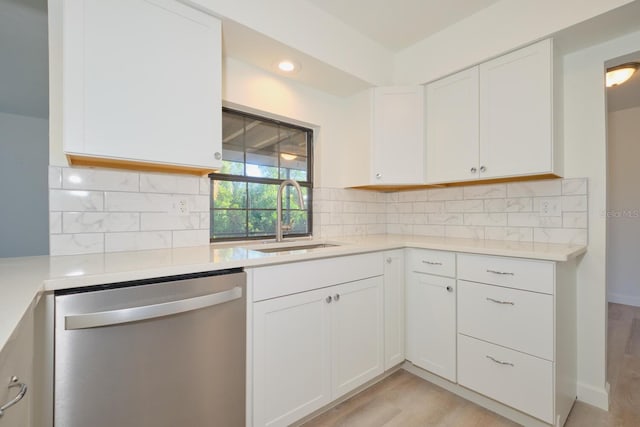 kitchen with sink, stainless steel dishwasher, backsplash, light hardwood / wood-style floors, and white cabinets